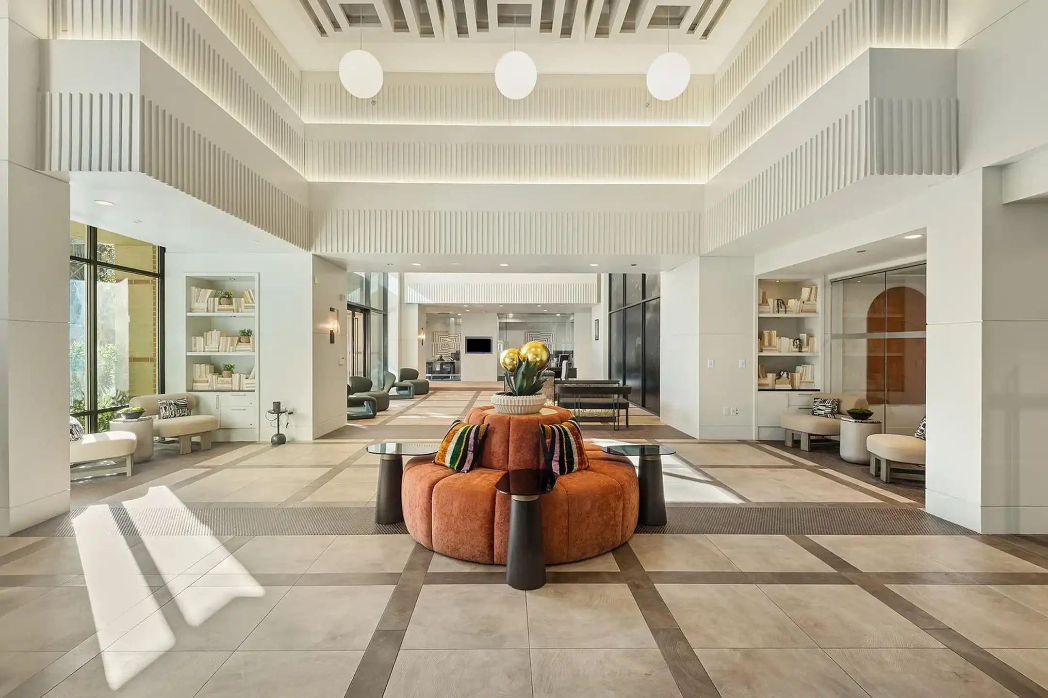 This lobby is a masterclass in Modern Art Deco, where soaring, tiered architecture meets residential-style luxury. The space is defined by dramatic vertical fluting and integrated cove lighting that carves out a high-volume, rhythmic ceiling, all set against a clean, gallery-white backdrop.