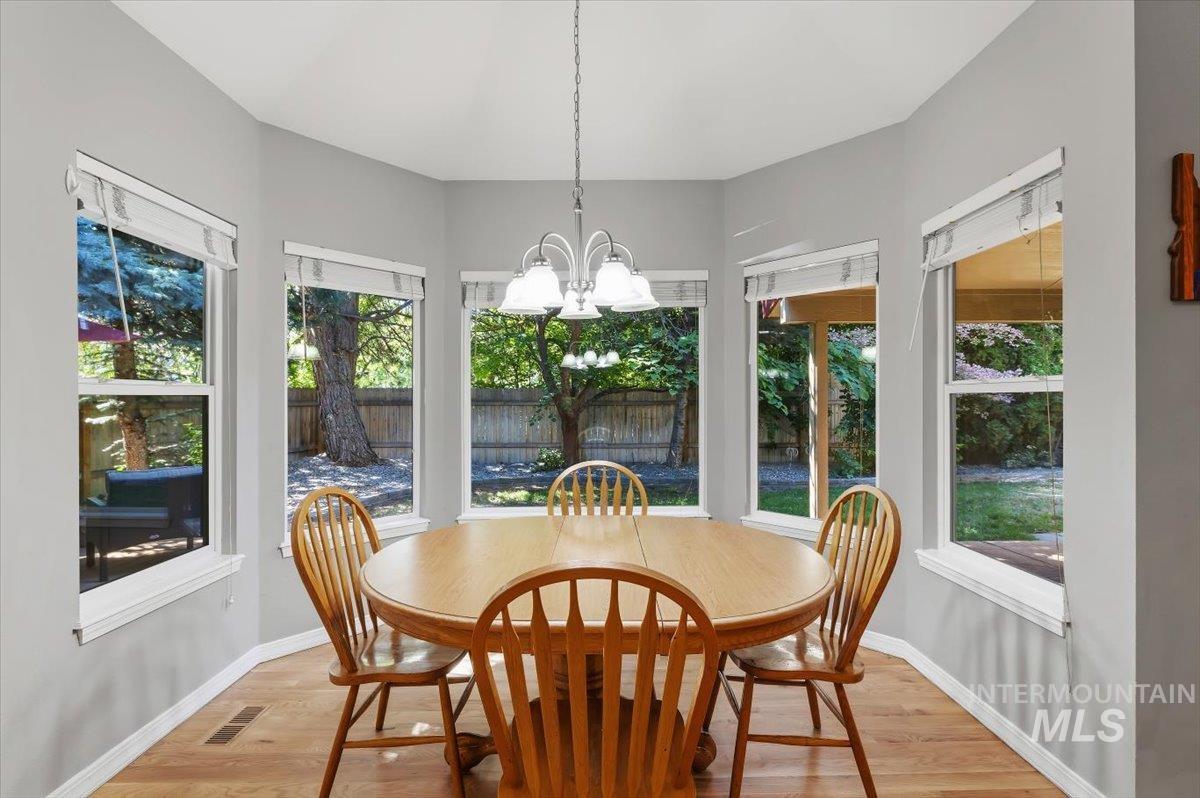 8001 West Innsbrook Court Boise, ID 83704 - Photo 14 of 39 Bay window alcove featuring five windows, light gray walls, wood-finish flooring, and a multi-light chandelier