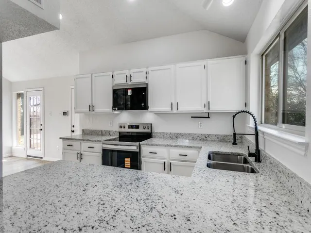 a kitchen with granite countertop a stove sink microwave and refrigerator