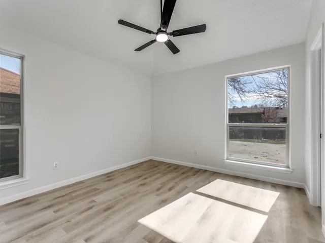 an empty room with wooden floor fan and windows