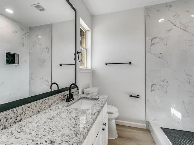 a bathroom with a granite countertop sink a toilet and shower