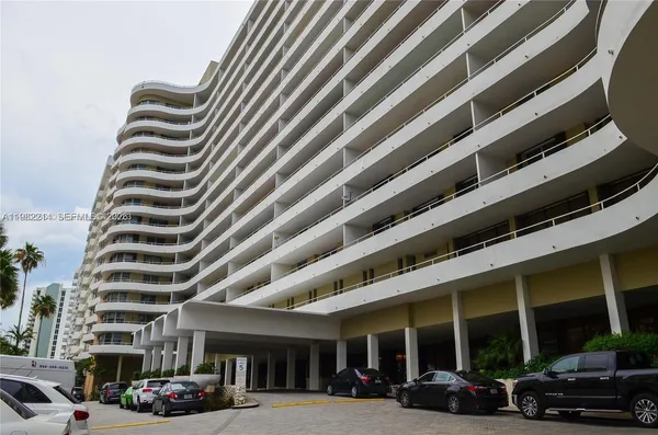 a front view of a building with lots of cars and trees