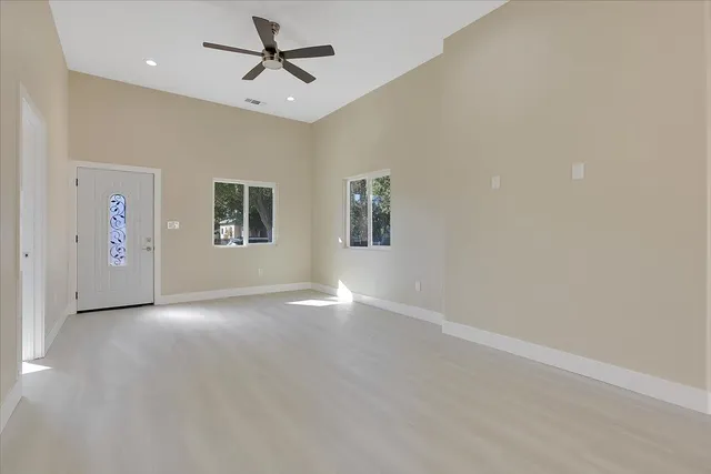 an empty room with chandelier fan and windows