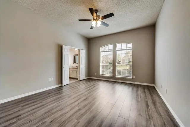 an empty room with wooden floor chandelier fan and windows