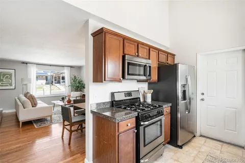a kitchen with stainless steel appliances granite countertop a stove top oven a sink dishwasher a dining table and chairs with wooden floor