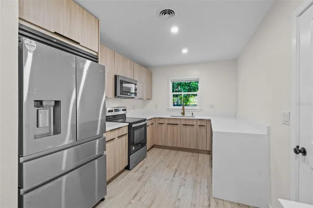 a kitchen with a refrigerator stainless steel appliances wooden floor and window