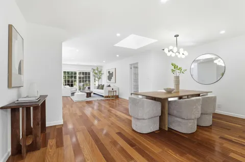a living room with kitchen island a dining table wooden floor and a large window