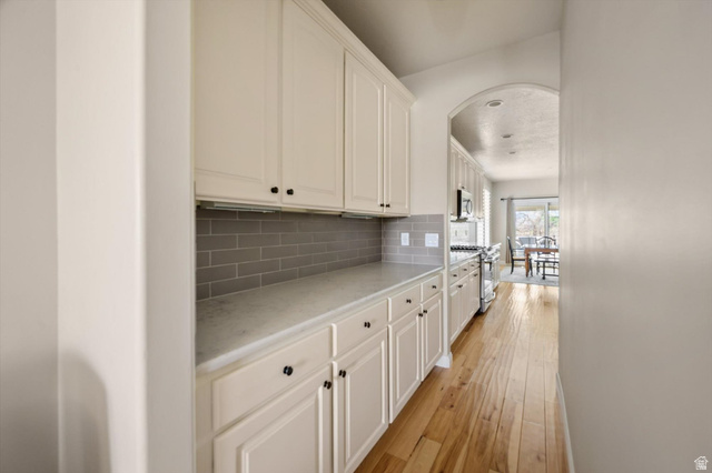 1456 Firelight Way Sandy, UT 84092 - Photo 4 of 22 Kitchen featuring light countertops, light wood finished floors, white cabinetry, arched walkways, and stainless steel appliances