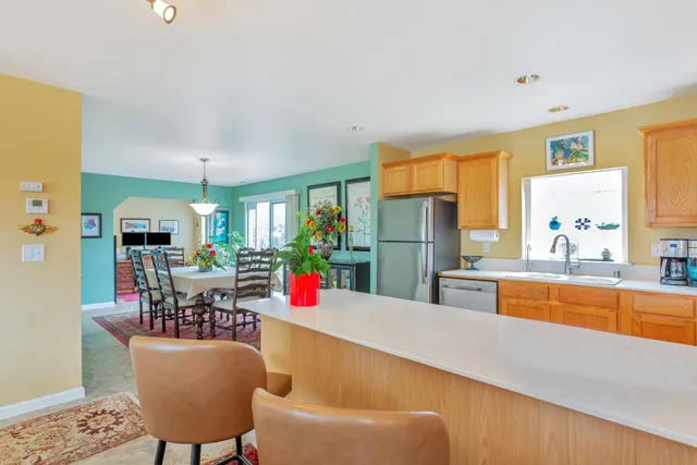 a kitchen with stainless steel appliances granite countertop a refrigerator a sink dishwasher and a dining table with garden view