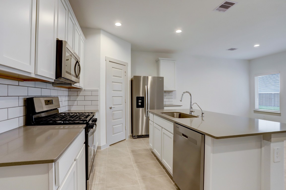 29866 Wildcat Way Katy, TX 77494 - Photo 5 of 25 Stylish modern kitchen featuring sleek cabinetry, stainless steel appliances, and a large center island with seating and a built-in sink. The quartz countertops provide both durability and elegance, while the subway tile backsplash adds a timeless touch. Ample counter space and storage make meal preparation easy, and the open layout allows the kitchen to flow naturally into the living and dining areas, making it perfect for cooking, entertaining, and gathering with family.