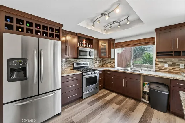 a kitchen with stainless steel appliances granite countertop a refrigerator a sink dishwasher a stove and white cabinets with wooden floor