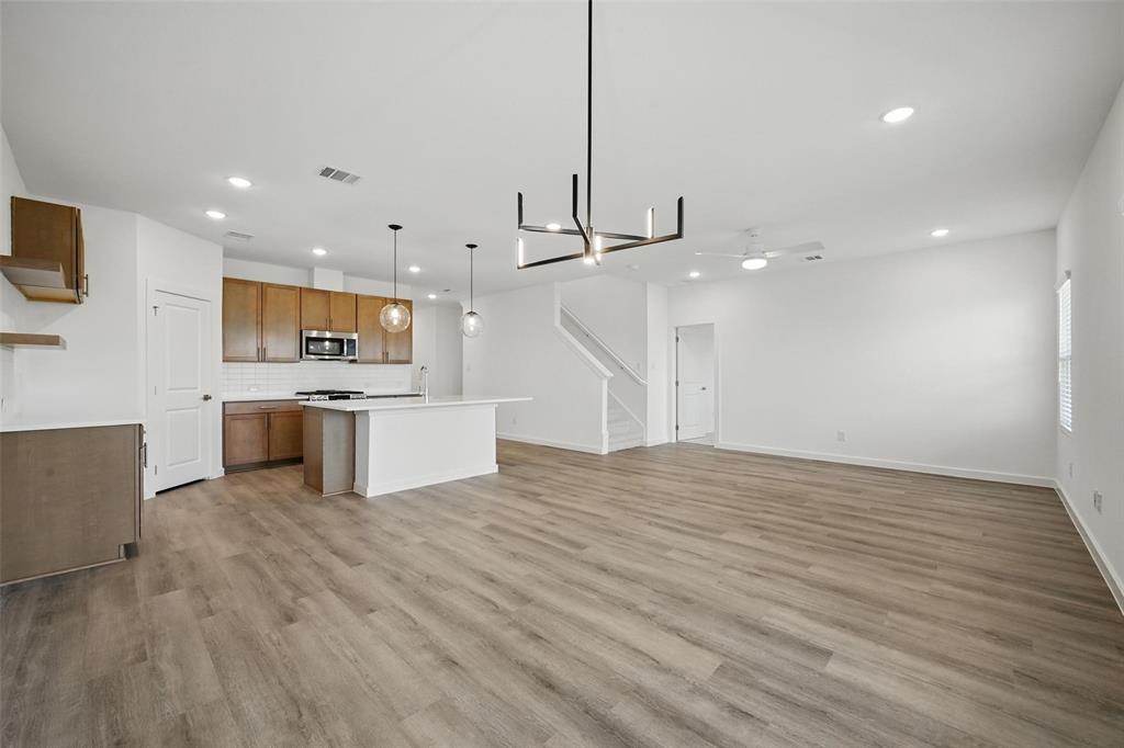 1413 Richardson Street Howe, TX 75459 - Photo 10 of 30 Open-concept living area featuring wood-finish flooring throughout, a modern kitchen island with seating, pendant lighting, recessed ceiling lights, and a contemporary chandelier