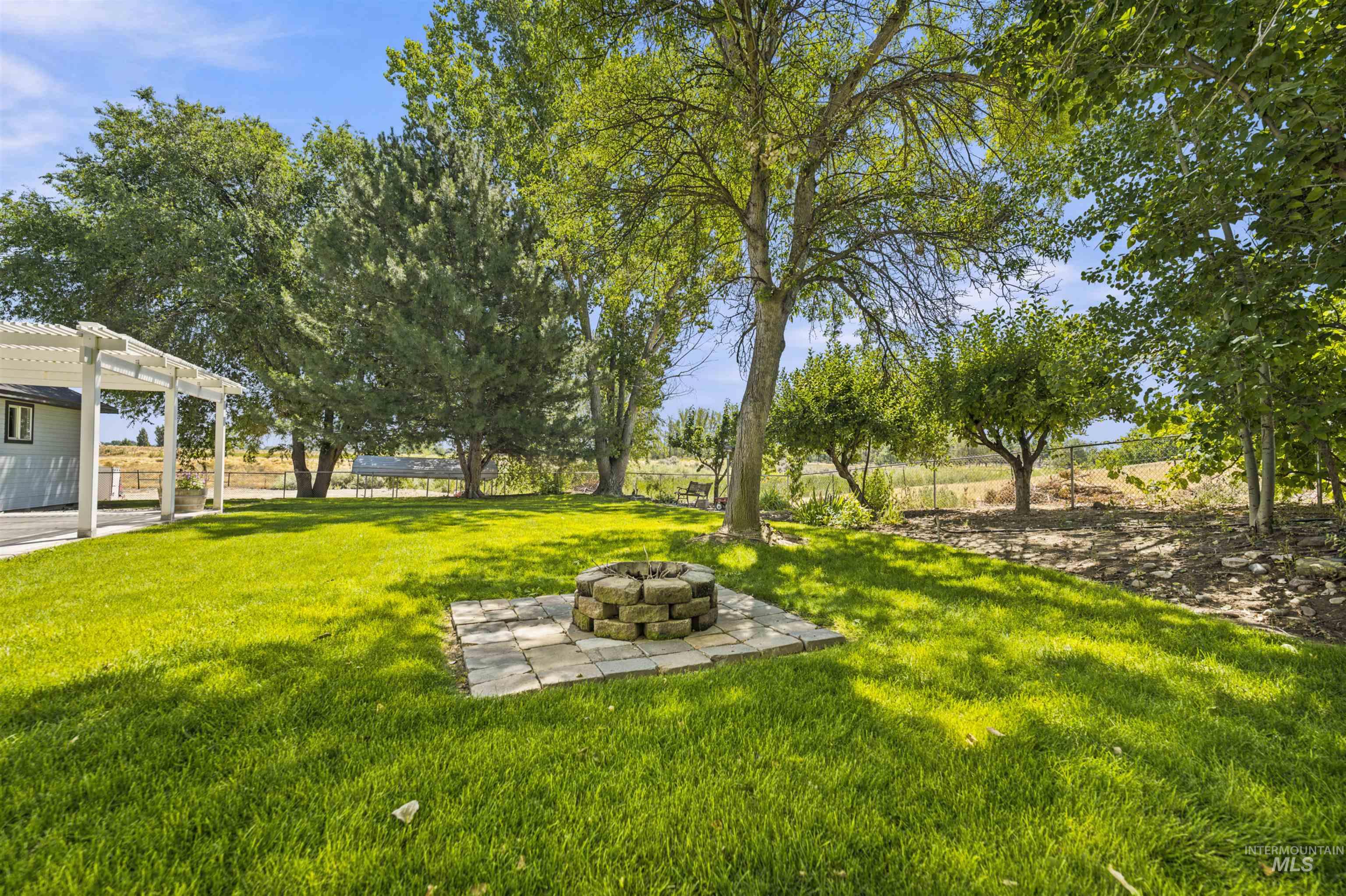 24864 Coventry Drive Caldwell, ID 83607 - Photo 40 of 49 Expansive lawn featuring a stone fire pit on paver stones, mature trees, and a covered patio area with a white pergola structure