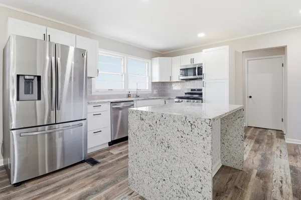 a kitchen with stainless steel appliances granite countertop a refrigerator a stove a sink and white cabinets with wooden floor