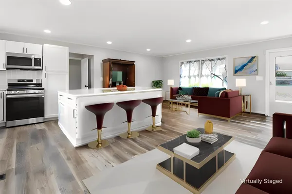 a living room with stainless steel appliances furniture a rug kitchen view and a window