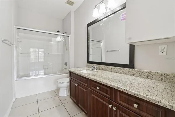a bathroom with a granite countertop sink a toilet a mirror and shower