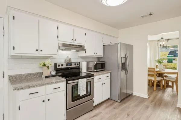 a kitchen with stainless steel appliances granite countertop a refrigerator stove and white cabinets with wooden floor