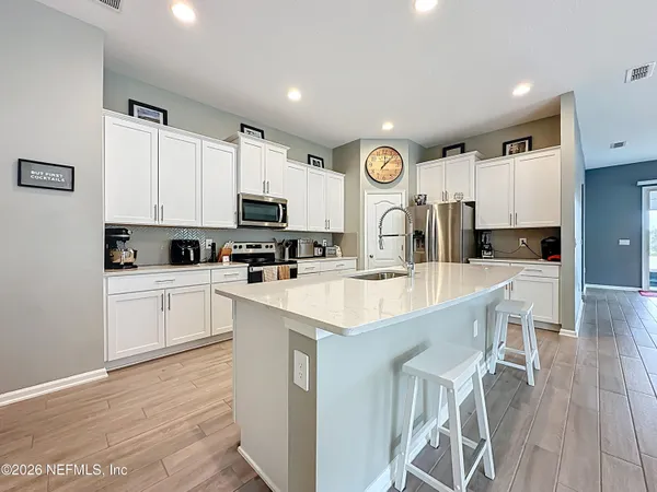 a kitchen with stainless steel appliances kitchen island granite countertop a stove a sink a refrigerator and white cabinets with wooden floor