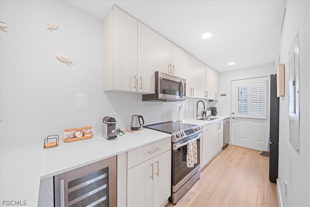 72 7th Street South, Unit 112 Naples, FL 34102 - Photo 8 of 28 a kitchen with a sink dishwasher a refrigerator and white cabinets with wooden floor