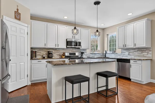 a kitchen with stainless steel appliances granite countertop a stove a sink dishwasher a refrigerator and white cabinets with wooden floor