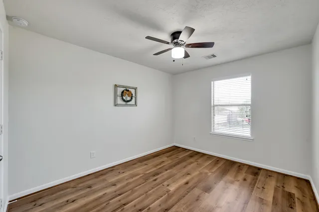 a view of empty room with wooden floor and fan