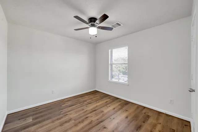 an empty room with wooden floor fan and windows