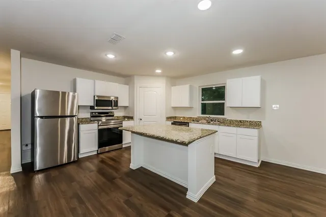 a kitchen with granite countertop a stove top oven a sink a refrigerator and white cabinets with wooden floor