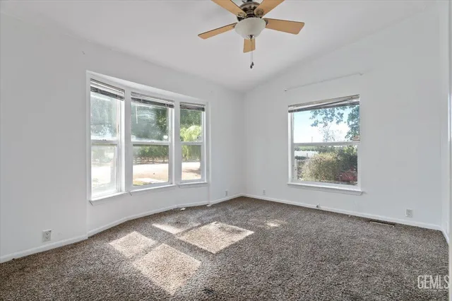 an empty room with chandelier fan and windows