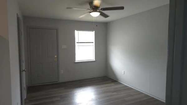 an empty room with wooden floor a ceiling fan and windows