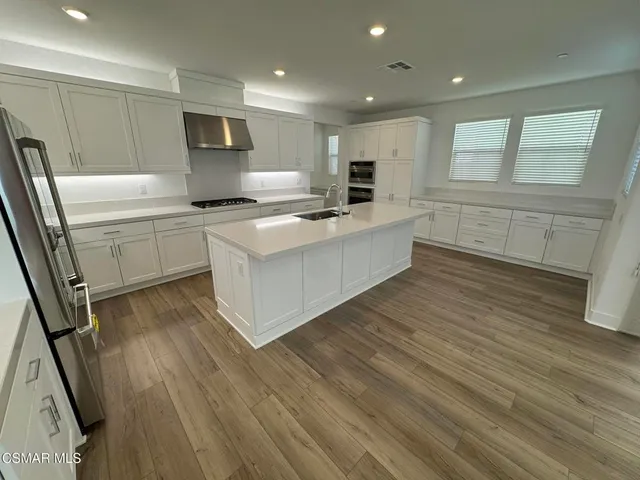 a large kitchen with stainless steel appliances a large counter top a stove a sink and a refrigerator