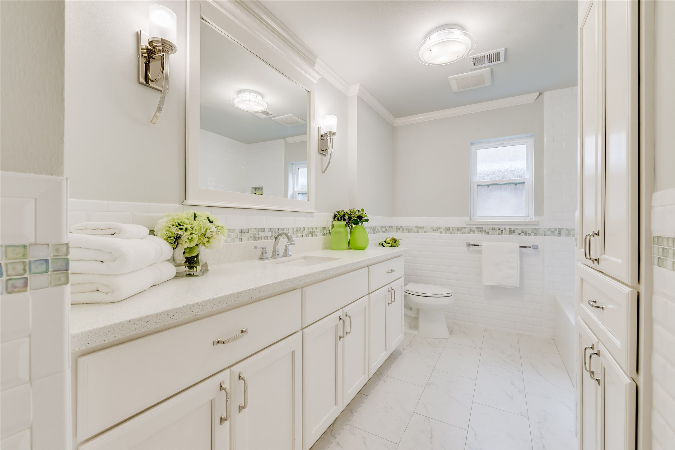 1010 Thornton Road Houston, TX 77018 - Photo 23 of 27 This bathroom features a clean, modern design with white cabinetry and tiled floors. It includes a spacious vanity, a large mirror, and elegant light fixtures. The soft, neutral colors create a bright and inviting atmosphere.