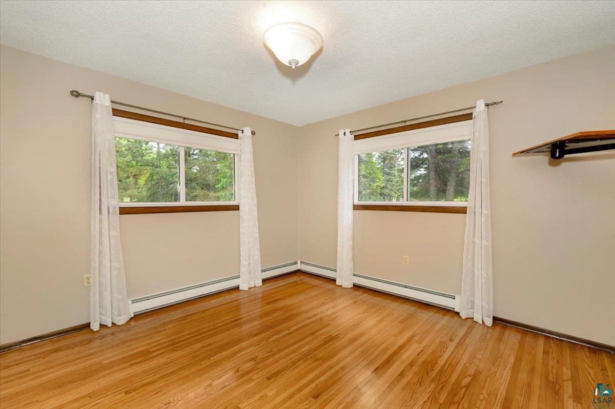 5219 West Arrowhead Road Hermantown, MN 55811 - Photo 11 of 35 Empty room with a wealth of natural light, a baseboard radiator, and light hardwood / wood-style flooring