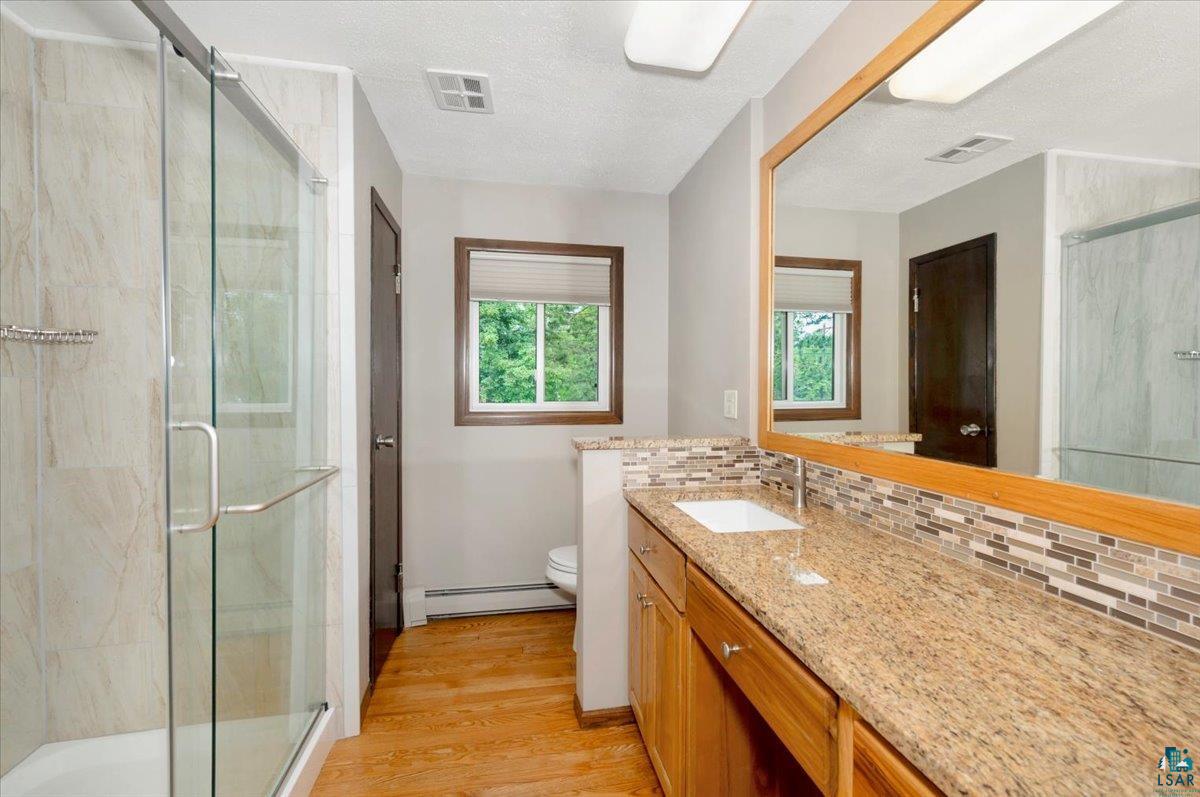 5219 West Arrowhead Road Hermantown, MN 55811 - Photo 12 of 35 Bathroom with baseboard heating, hardwood / wood-style floors, tasteful backsplash, large vanity, and toilet