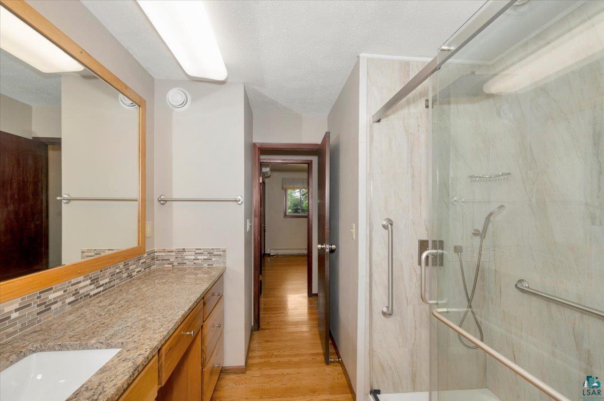 5219 West Arrowhead Road Hermantown, MN 55811 - Photo 13 of 35 Bathroom featuring a shower with shower door, hardwood / wood-style flooring, backsplash, and vanity