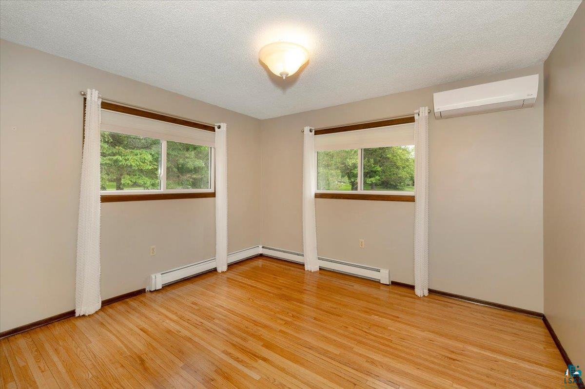 5219 West Arrowhead Road Hermantown, MN 55811 - Photo 14 of 35 Empty room featuring a wall mounted AC, light hardwood / wood-style floors, and a textured ceiling