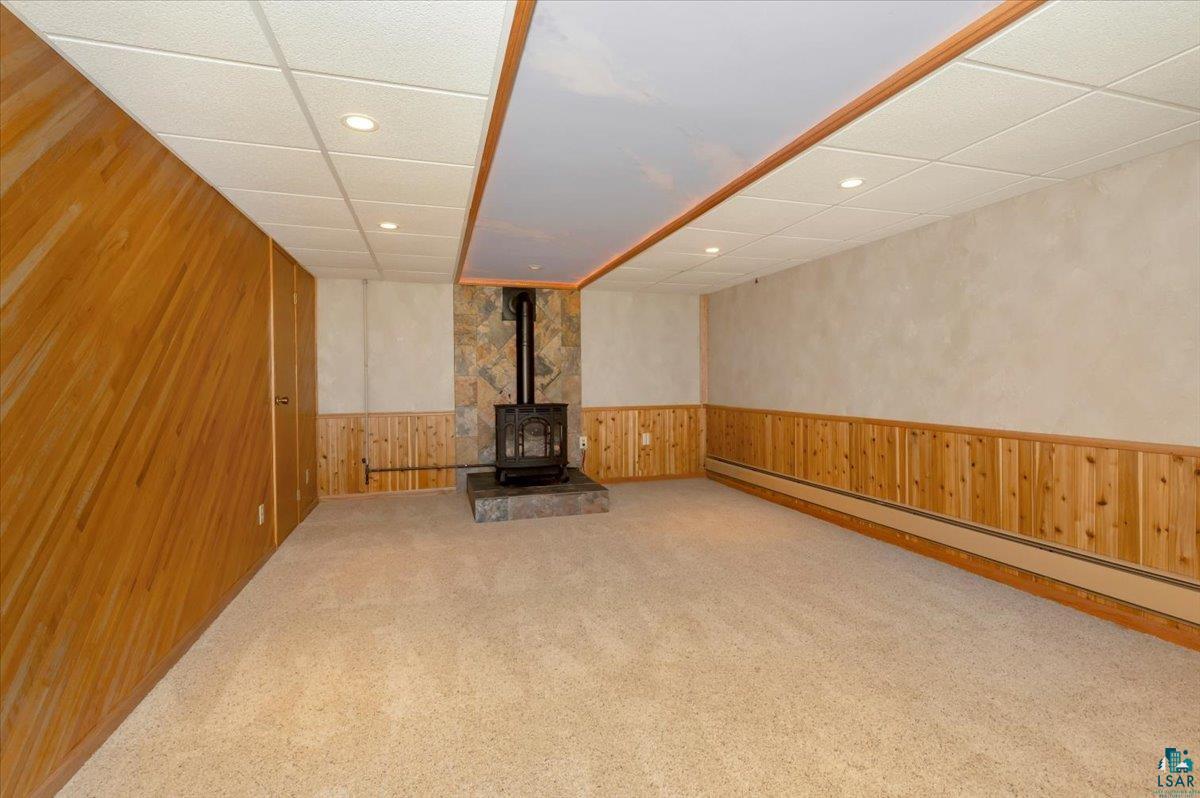 5219 West Arrowhead Road Hermantown, MN 55811 - Photo 20 of 35 Basement featuring carpet floors, baseboard heating, a paneled ceiling, a wood stove, and wood walls