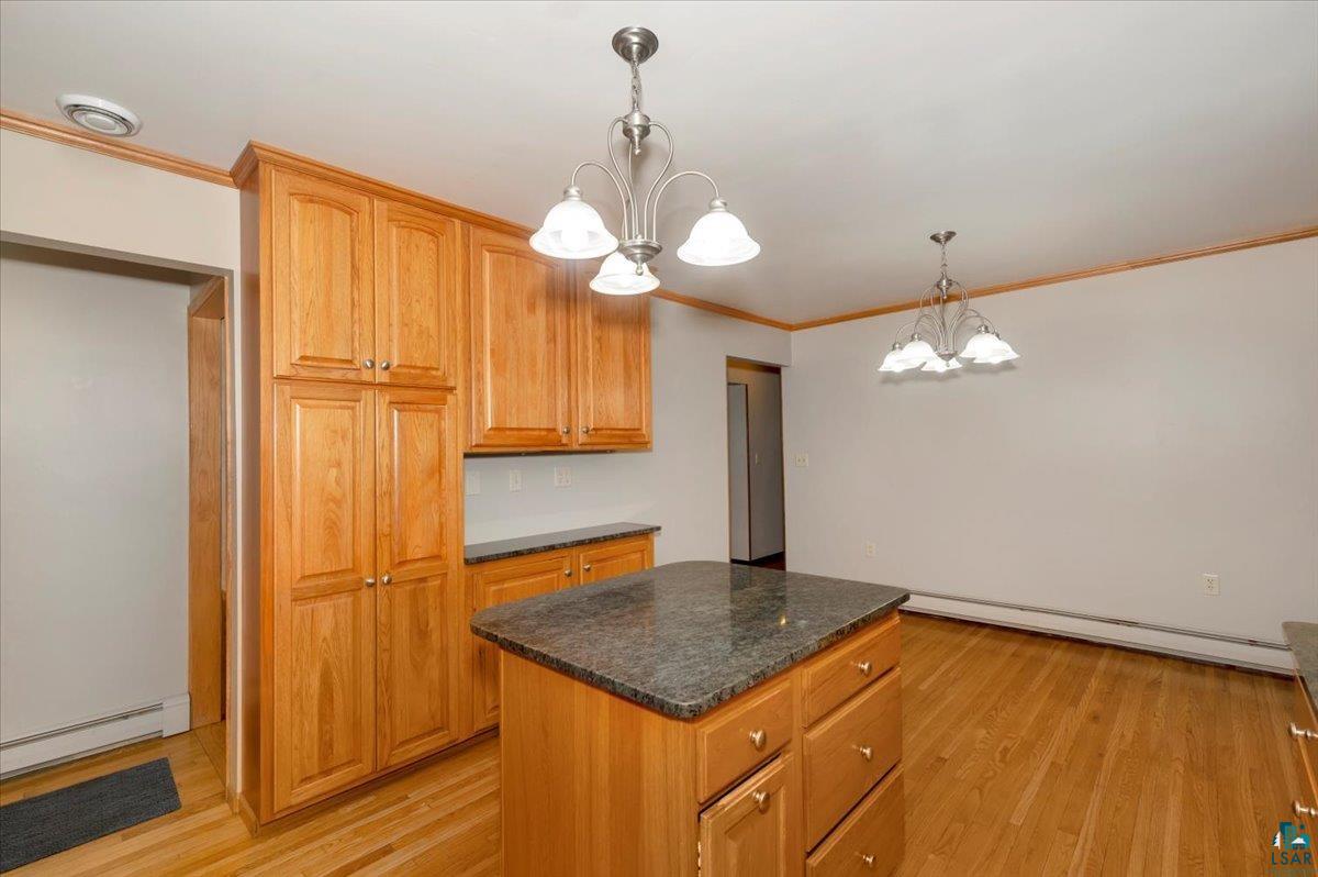 5219 West Arrowhead Road Hermantown, MN 55811 - Photo 4 of 35 Kitchen featuring light wood-type flooring, a notable chandelier, hanging light fixtures, a center island, and a baseboard radiator