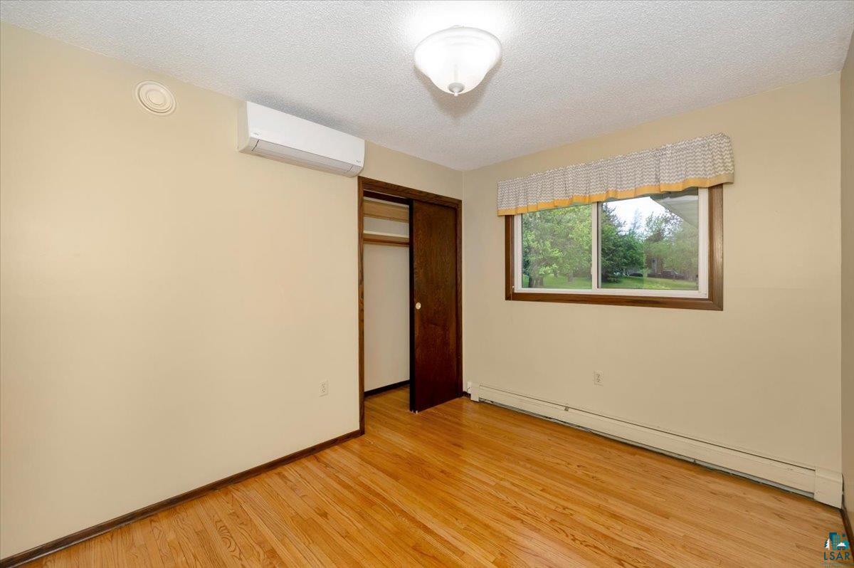 5219 West Arrowhead Road Hermantown, MN 55811 - Photo 8 of 35 Unfurnished bedroom featuring a closet, an AC wall unit, a baseboard heating unit, light wood-type flooring, and a textured ceiling