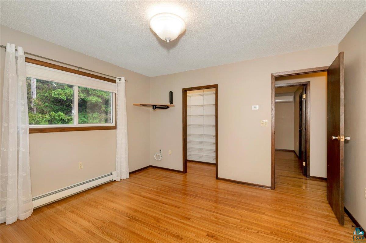 5219 West Arrowhead Road Hermantown, MN 55811 - Photo 10 of 35 Unfurnished bedroom with baseboard heating, light hardwood / wood-style flooring, and a textured ceiling