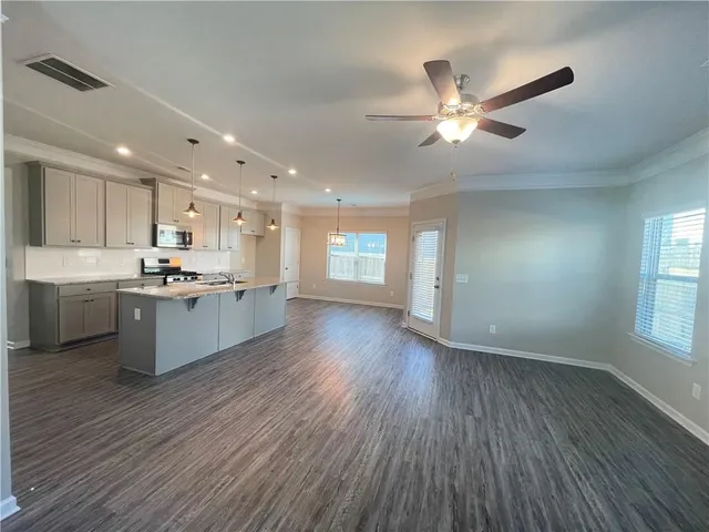 a view of an empty room and kitchen with wooden floor and a window