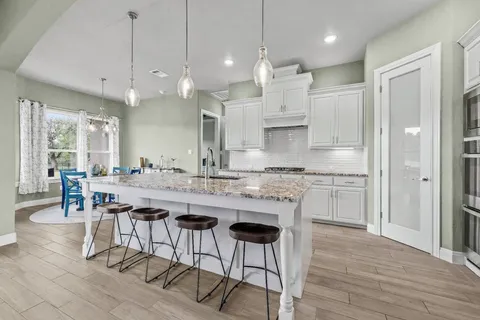 a kitchen with stainless steel appliances granite countertop a stove a sink a kitchen island and chairs with wooden floor