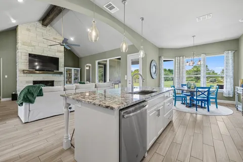 a kitchen with stainless steel appliances granite countertop a stove top oven a sink dishwasher a dining table and chairs with wooden floor