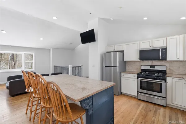 a kitchen with stainless steel appliances a stove a sink a microwave a refrigerator white cabinets and wooden floor