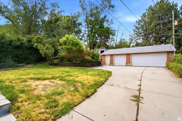 1341 29th Street Ogden, UT 84403 - Photo 28 of 37 Concrete driveway leading to a detached garage with two white garage doors, an additional access door, and a light-colored shingle roof