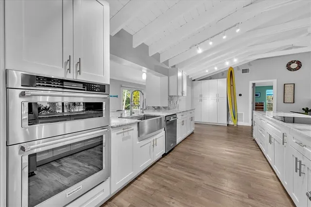 a white kitchen with granite countertop a stove top oven a sink and dishwasher