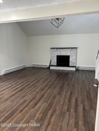a view of an empty room with wooden floor and a fireplace