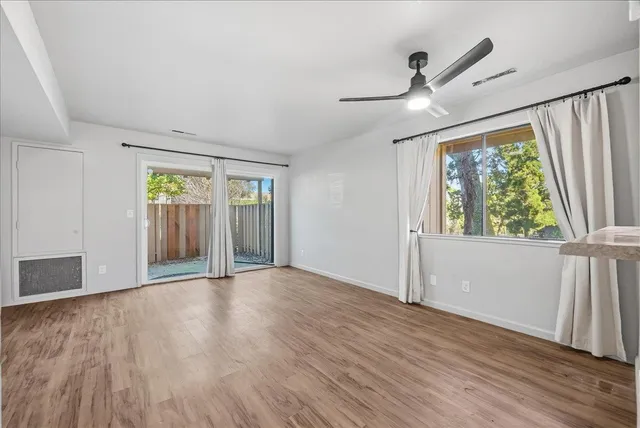an empty room with wooden floor fan and windows