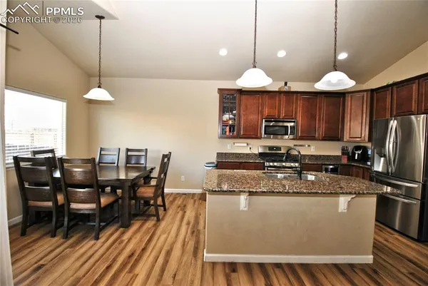 a kitchen with stainless steel appliances granite countertop a stove a refrigerator a kitchen island a dining table and chairs with wooden floor