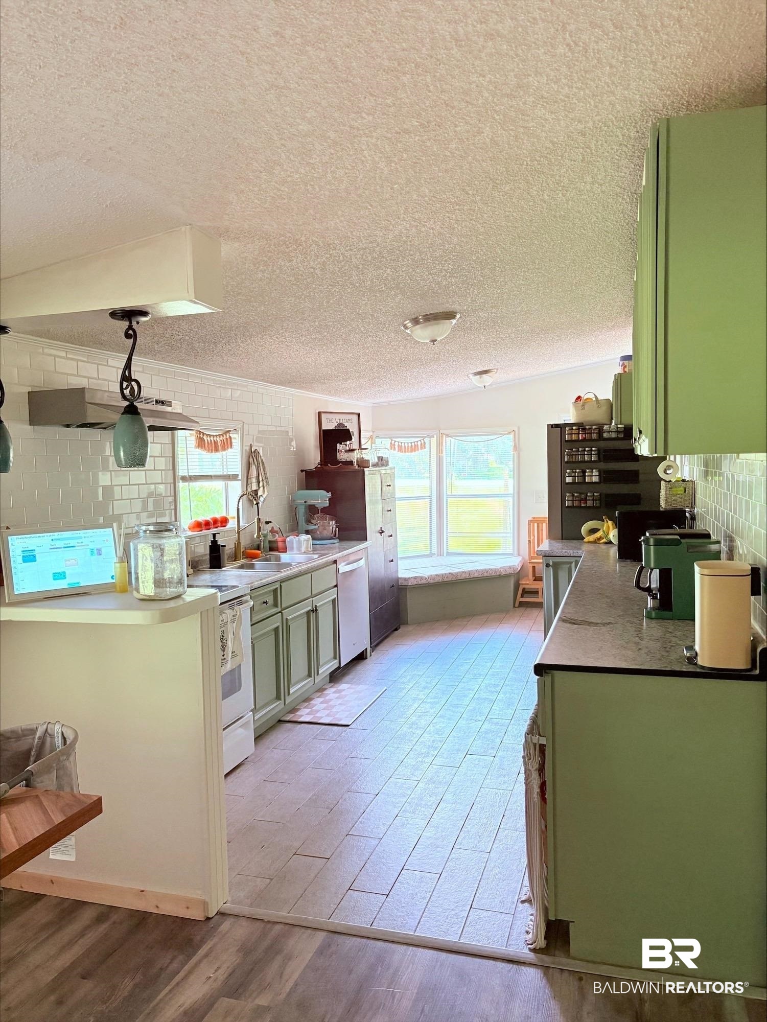 12020 Bay Road West Foley, AL 36535 - Photo 9 of 30 Kitchen featuring green cabinetry, dishwashing machine, a textured ceiling, light wood finished floors, and backsplash