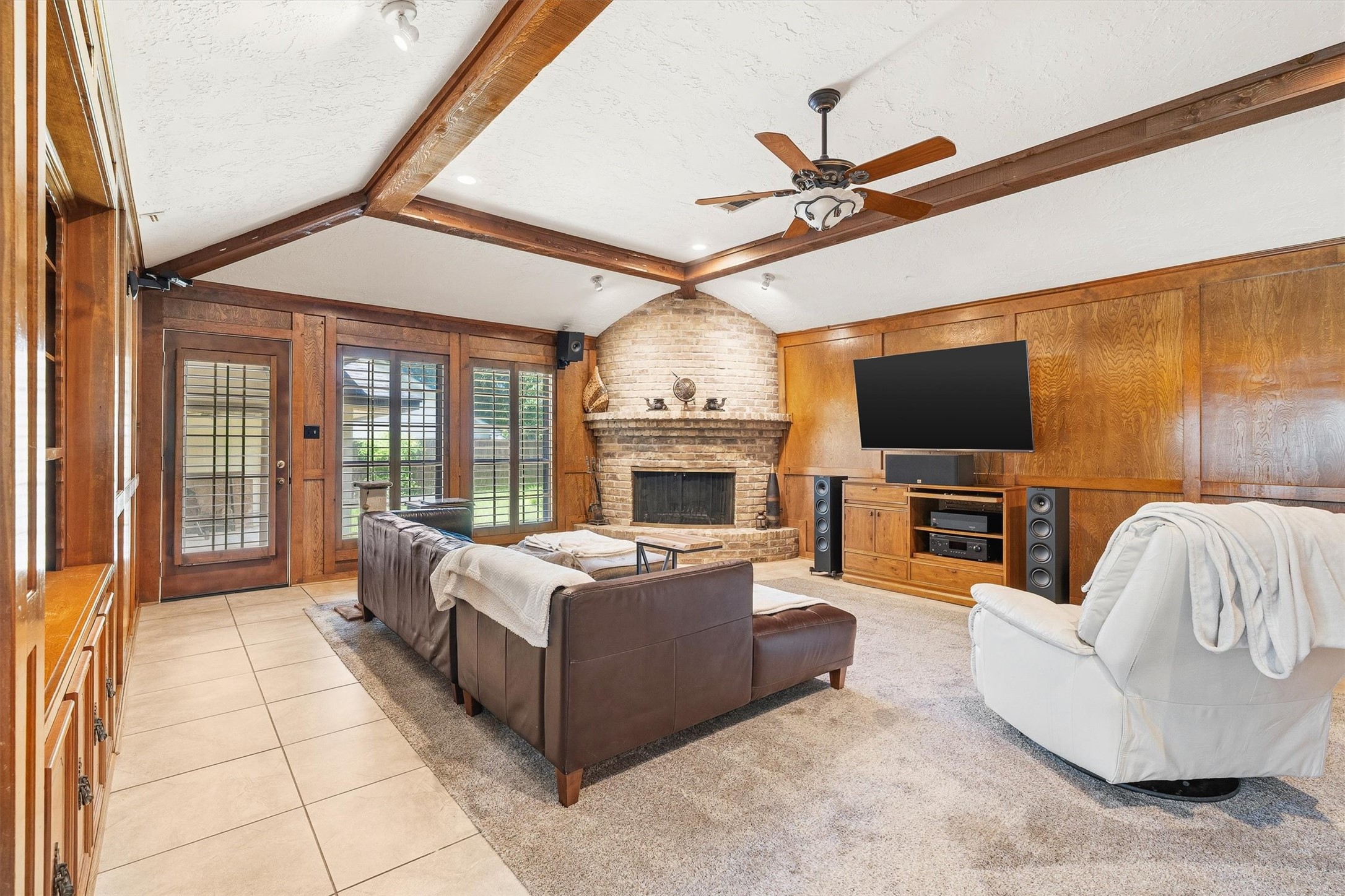 826 North Rivershire Drive Conroe, TX 77304 - Photo 6 of 46 At the heart of the home, this living room delivers — vaulted beamed ceilings, a floor-to-ceiling brick fireplace, wood-paneled walls, and French doors that open directly to the backyard. This is the room you gather in, entertain in, and never want to leave.